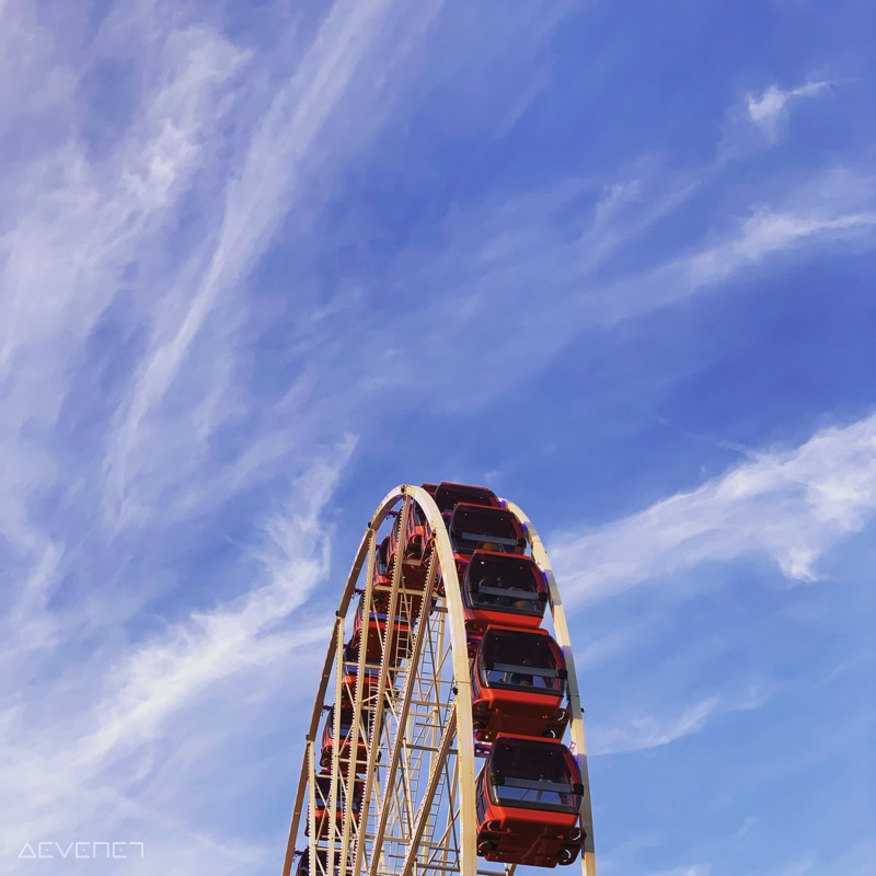 Haut d’une grande roue avec nacelles rouge et noir sous un ciel bleu.