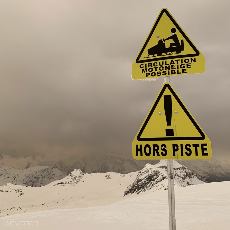 Montage enneigée et orangée, avec panneaux “Attention hors piste” et “Circulation motoneiges possible”.