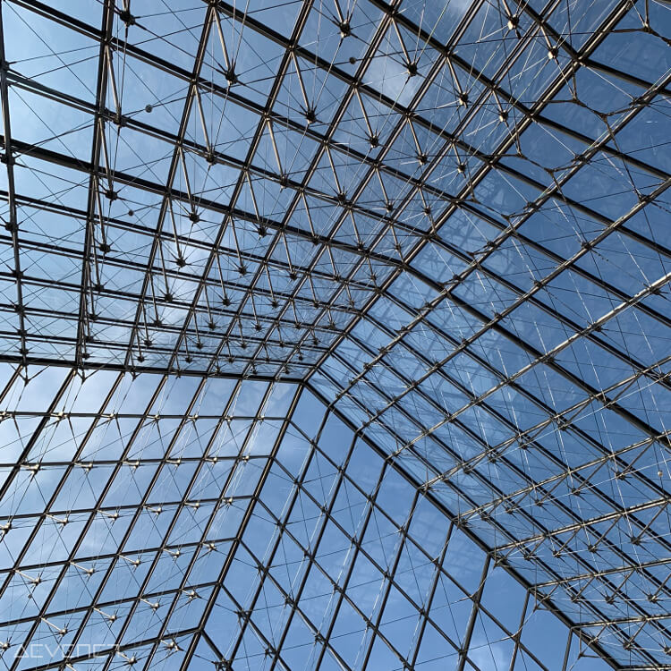 Nombreux carreaux de verres mêlés à une structure en acier, donnant vers le ciel bleu parsemé d’une trace d’un nuage.