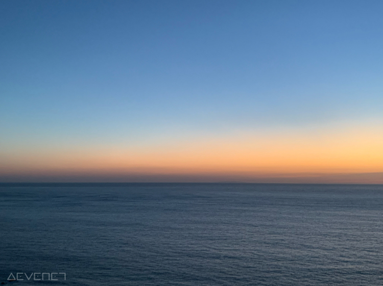 Coucher de soleil sur la mer. Bleu clair lisse en haut, couleurs orangé au milieu, et bleu foncé avec quelques remous en bas.