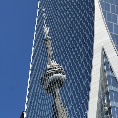 Reflet de la Tour CN de Toronto sur la façade vitrée et géométrique d’un gratte-ciel.