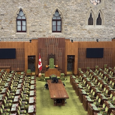Vue d’ensemble de la Chambre des communes du Canada avec ses sièges verts et le drapeau canadien.
