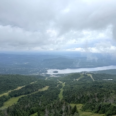 Vue panoramique depuis le sommet du mont Tremblant sur une forêt verdoyante et un lac.