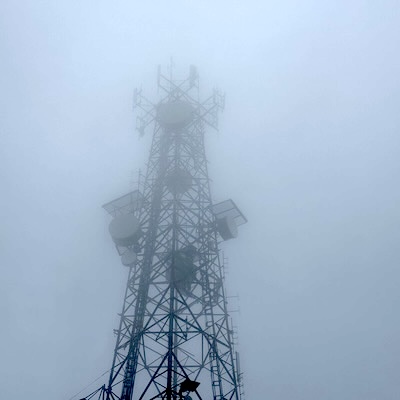 Tour de télécommunication métallique plongée dans un épais brouillard au sommet d’une montagne.
